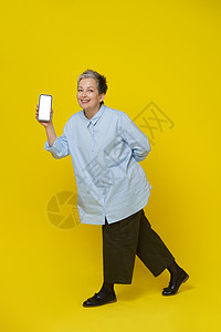 穿着蓝衬衫和棕色长裤的漂亮女性被黄色背景隔离 Mocto app广告 Mockup产品布置撰稿人金融上网人士白发退休网上购物药片图片