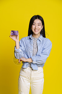 微笑的亚洲女孩手里拿着信用卡 借记卡 身穿蓝色衬衫的亚洲女孩 银行卡样机在黄色背景下被隔离 电子银行概念 电子商务概念图片