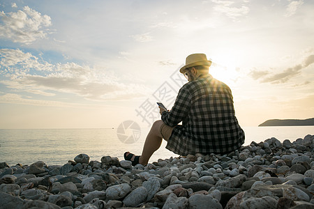 在阳光明媚的日子里 坐在海滩露台上的智能手机男子的后侧视图 背景外有复制空间  假期或自由职业者或社交网络概念帽子旅行热带工作技图片