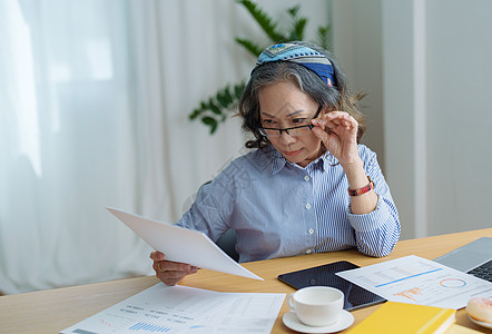 老年妇女手持重要文件核实纸上笔记真伪的画像老板秘书女士审计工作笔记本顾问金融公用事业文档图片