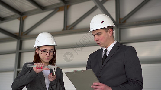 在建筑工地戴头盔并携带文件的男女青年 身着衣物的商务人士用电动卡利帕测量细节图片