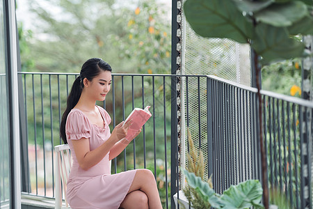 年轻美丽的女士坐着 在阳台上读一本书花园女性工作阅读椅子公寓成人绿色闲暇房子图片