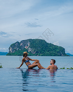 一对欧洲男人和亚洲女人在泰国的无边泳池里眺望大海 在泰国享受豪华假期酒店游泳飞溅女孩旅行快乐天线奢华女士晴天图片
