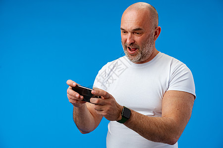 快乐的中年男人拿着手机 在蓝背景下欢乐地握着电话幸福成人短信生意衬衫老板工作室人士工作男性图片