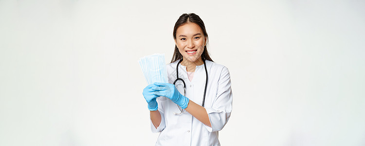 微笑的女性女医生 显示医疗面罩的护士 身穿无消菌橡胶手套 站在白底背上面具工人感染症状医院疾病女士诊所实习生情况图片