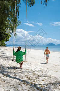泰国普吉岛附近热带岛屿纳卡岛海滩上的一对男女 海滩秋千上的女人和散步的男人自由天堂女性中岛蜜月太阳镜海洋女士旅行假期图片