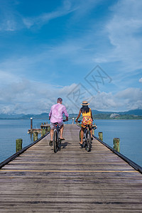 泰国普吉岛纳卡岛一座带木码头的热带岛屿上骑着自行车的男人和女人 一对男女夫妻自由女性快乐蓝色假期运输奢华女士情侣图片
