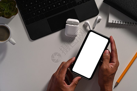 上面看到商务人士手持智能电话 在办公桌用空屏幕显示图片