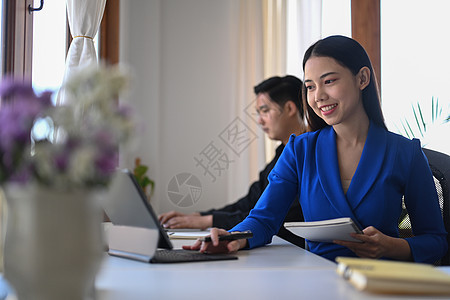 有吸引力的女商务人士在与办公室同事坐在一起时 用计算机平板电脑工作着图片