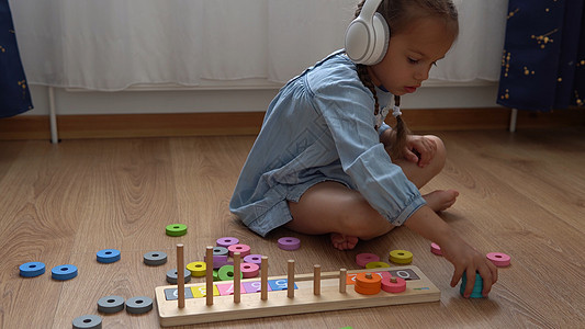 快乐的学龄前没牙小女孩玩彩色木制玩具 孩子们通过在家玩教数字来学习数数 听音乐的孩子在大白色耳机 童年 教育电脑微笑卧室动作动物图片