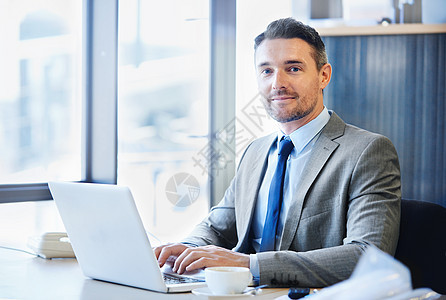 我从不离工作站远 办公室里一个微笑的商务人士在笔记本电脑上工作的肖像图片