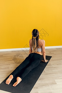 一位身穿运动服的美丽年轻女子在黄色背景的运动垫上练习瑜伽的侧视图 伸展背部和腿部肌肉 瑜伽姿势成人运动装减肥福利身体灵活性健身房图片