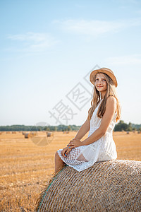 穿着白裙子和草帽的阳性女孩 坐在农业田里的稻草泥上图片