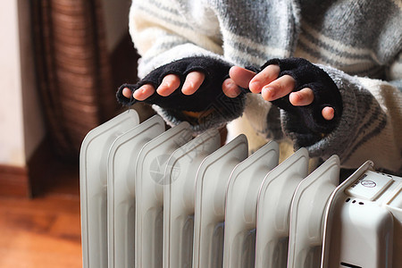 在冬季用家用便携式散热器在家中取暖的人的手供暖图片