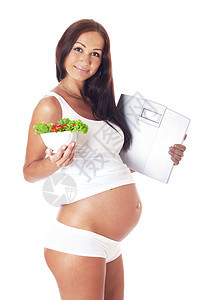 孕妇持有比例尺和吃沙拉母性维生素腹部食物怀孕幸福亲热称重器蔬菜女士图片
