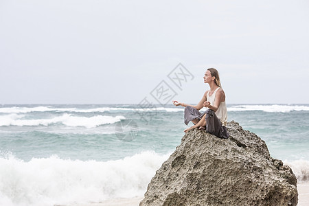 女孩坐在岩石边的海边 静坐着瑜伽女人的姿势海岸线平衡日落闲暇海滩头脑女士活力冥想宗教图片