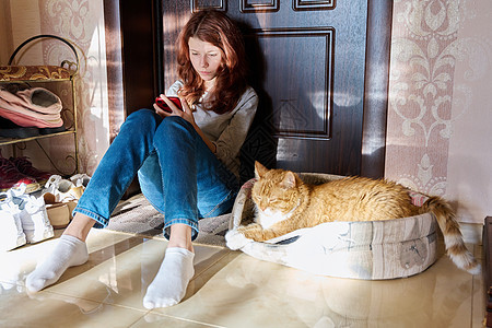 使用智能手机和睡宠物猫坐在家中地板上的十几岁女孩电话成人技术宠物互联网女士房间闲暇青春期青少年图片