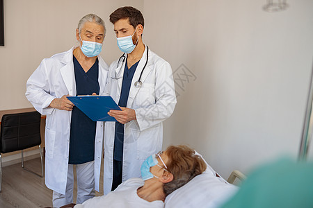 戴面罩的专业医生讨论病人的诊断问题 在医院病房中站立考试顾问治疗办公室治疗师女士写作职业男人疾病图片