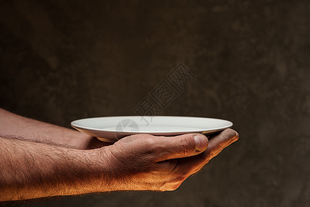 在黑暗背景 缺乏食物 饥饿概念下 男性手握空盘子饮食厨具服务粮食烹饪空白圆形午餐用具危机图片