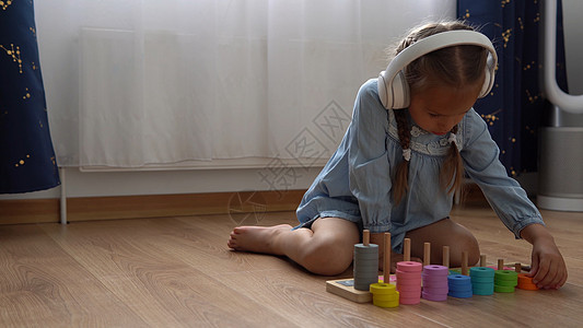 快乐的学龄前没牙小女孩玩彩色木制玩具 孩子们通过在家玩教数字来学习数数 听音乐的孩子在大白色耳机 童年 教育音乐婴儿女孩情感厨房图片