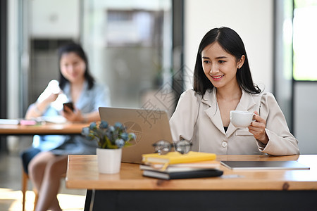 年轻的年青女性办公室工人拿着咖啡杯 用笔记本电脑工作图片