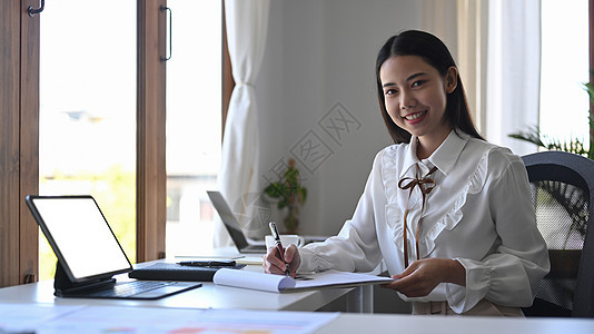 在明亮办公室用电脑平板电脑工作的年轻女商务人士愉快地工作图片