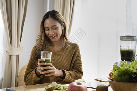 健康的年轻女子坐在厨房里时 拿着一杯新鲜有机冰淇淋的酒杯图片