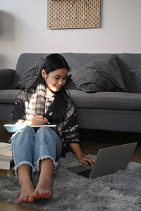 亚洲女孩坐在起居室的地板上 用笔记本电脑浏览互联网图片