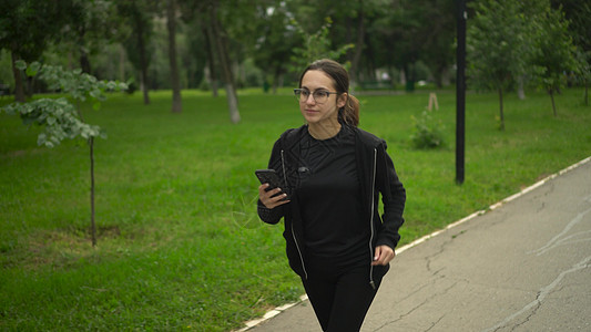 一位年轻女性手握着手机在慢跑并欢欣鼓舞 带眼镜的亚洲女孩正在用电话移动中的应用程序来赚钱图片