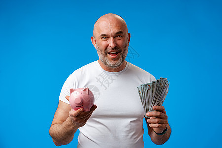 中年男子在蓝背景下持有小猪银行小猪银行现金存钱罐成功收益储蓄硬币金融经济图片