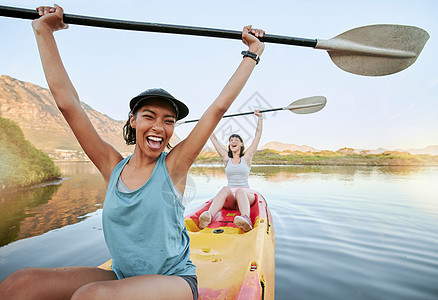 画像两个不同的年轻女子在湖上划独木舟时欢呼和庆祝 兴奋的朋友在度假或度假时在河上享受划船和皮划艇 在周末度假中获胜背景图片