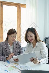 两位年轻亚洲女商务人士的肖像 他们使用带有计算器和文件的平板电脑来规划营销策略和投资 以从客户那里获利图片