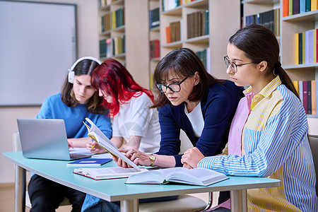 青少年学生群体和在图书馆书桌上的师范学习桌子中学女士多样性教科书学校微笑小学生教育女性图片