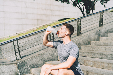 坐在楼梯上 在体育训练后放松 在夏季城市街道做运动时喝着饮用水的瓶子 (掌声 )图片