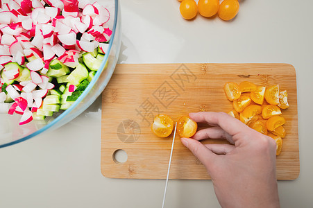 蔬菜沙拉手写字近身女性手在家中厨房切菜板上切割新鲜黄樱桃西红柿厨师桌子食物蔬菜营养饮食烹饪沙拉黄色绿色背景
