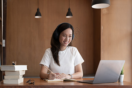 快乐的亚洲女人坐在家里的办公桌前 在电脑上在线写作学习 微笑的年轻混血女性在笔记本电脑上远程工作 在网上学习课程 教育 学习理念图片