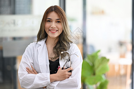 带着双臂站立的迷人的亚洲女医生 向镜头微笑着笑图片