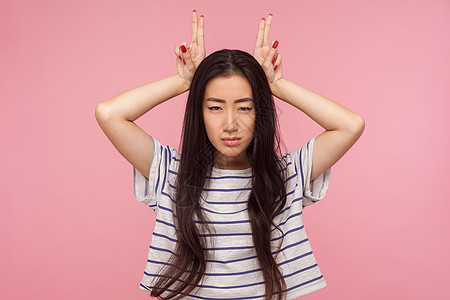 粉红色背景的亚洲年轻女性肖像防御黑发愤怒手指情感危险女孩手势t恤牛角图片