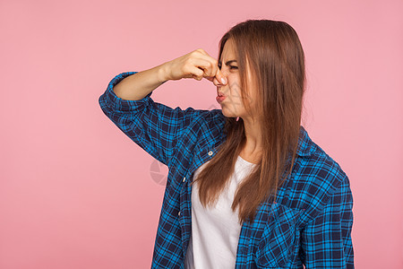 粉红色背景的年轻情感女性的肖像女士斥力厌恶衬衫格子黑发鼻子手指呼吸香气图片