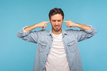 青蓝背景的年轻情感男子的肖像头痛噪音警报压力蓝色听力男人男性耳朵手指图片