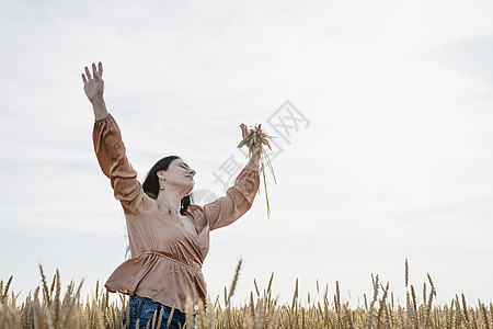 身穿米色衬衣的中成年妇女站在小麦田上 背景 背面和背面有日出草地大麦幸福晴天阳光女士植物裙子快乐帽子图片