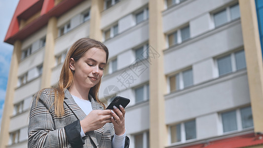 一个女孩穿过镇子 看她的智能手机学生阅读工作室互联网微笑牙齿新闻毛衣女士技术图片