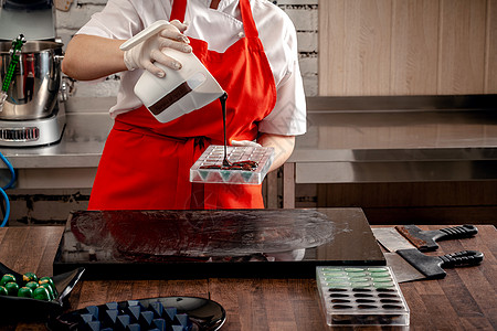 一位穿红色制服和白色无菌手套的美食妇女用餐桌上的牛奶巧克力来做一套多彩巧克力工作室软糖烘烤厨师女士食用糖果商糕点面包师房子图片