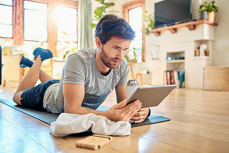 一名健康的年轻白人男子在家中锻炼休息时使用数字平板设备 使用健身应用程序 浏览社交媒体和观看在线锻炼教程的人男人肌肉地面学习成人图片