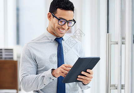 快乐的混血商务人士拿着和使用数字平板电脑站在办公室工作 一位心满意足的西班牙裔男性商务人士在工作时在数字平板电脑上键入电子邮件时图片