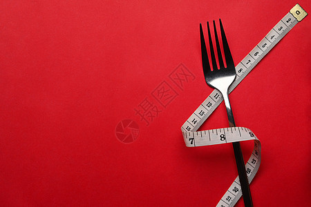 带有测量磁带的叉子在红色背景上 复制文本空间 健康生活方式概念图片