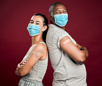 Covid 接种了非洲裔美国男子和混血女子背靠背站着 在有复制空间的工作室里 两个戴着外科口罩的人在红色背景下被隔离 显示手臂上图片