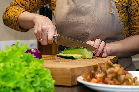 沙拉准备过程的特写视图 一个穿围裙的女人在木砧板上切黄瓜食物沙拉桌子烹饪木板女性厨房家庭手臂蔬菜图片