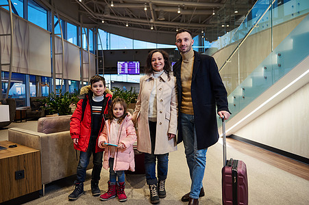 快乐的多民族家庭带着手提箱 站在国际机场出发航站楼的航班信息板旁 上面有时间表图片