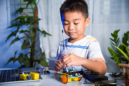 亚洲小男孩利用Arduino机器人车将能量和信号电缆插到传感器芯片上学校原型教育数学软件代码工程师技术活动创新图片